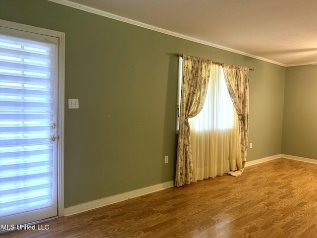 spare room featuring crown molding, a wealth of natural light, wood finished floors, and baseboards