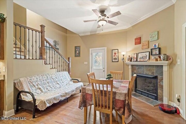 dining area with a tile fireplace, hardwood / wood-style flooring, ceiling fan, and ornamental molding