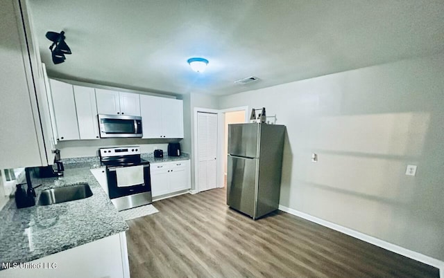 kitchen with white cabinets, light wood-type flooring, stainless steel appliances, sink, and light stone counters