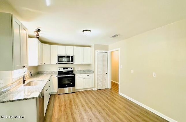 kitchen featuring stainless steel appliances, sink, white cabinetry, light stone counters, and light hardwood / wood-style floors