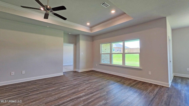 empty room featuring dark wood-style floors, a tray ceiling, visible vents, and crown molding