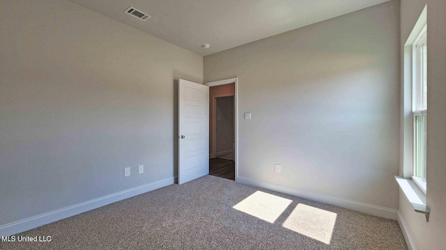 carpeted spare room with a wealth of natural light, visible vents, and baseboards