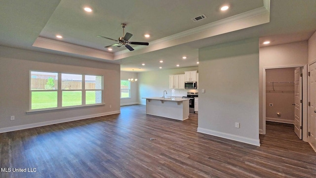 unfurnished living room with a tray ceiling, dark wood finished floors, and ornamental molding