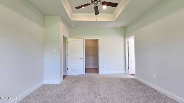 unfurnished bedroom with a tray ceiling, carpet, crown molding, a spacious closet, and baseboards