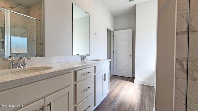 bathroom with double vanity, a sink, a shower stall, and wood finished floors