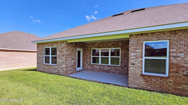 back of house with brick siding, a lawn, and roof with shingles