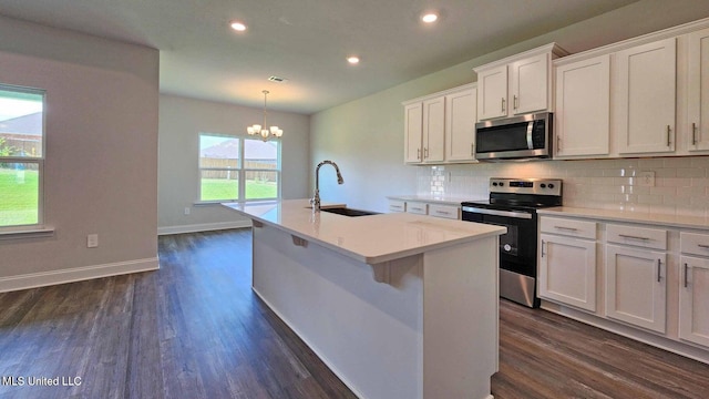 kitchen featuring dark wood finished floors, stainless steel appliances, decorative backsplash, a kitchen island with sink, and a sink