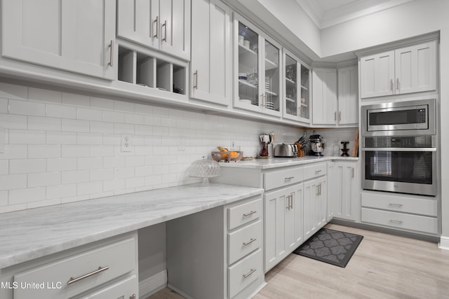 kitchen featuring light stone countertops, light hardwood / wood-style flooring, decorative backsplash, appliances with stainless steel finishes, and ornamental molding