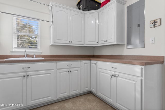 kitchen with electric panel, white cabinetry, and sink