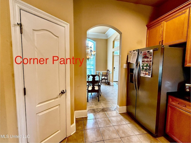 kitchen with dark countertops, stainless steel fridge, arched walkways, brown cabinetry, and light tile patterned floors