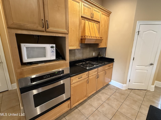 kitchen featuring premium range hood, light tile patterned flooring, decorative backsplash, appliances with stainless steel finishes, and dark countertops