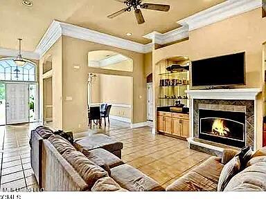 living area featuring light tile patterned floors, a warm lit fireplace, crown molding, and a ceiling fan