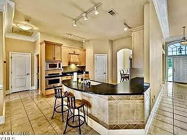 kitchen featuring dark countertops, visible vents, light tile patterned floors, arched walkways, and stainless steel appliances