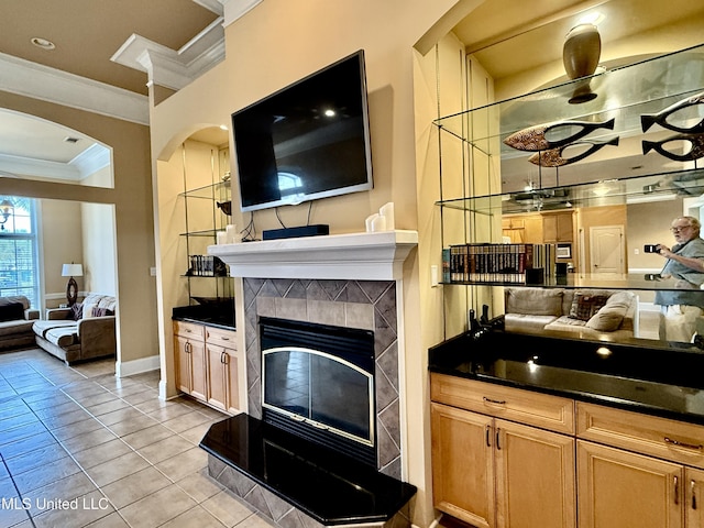 living room with light tile patterned floors, baseboards, arched walkways, a tile fireplace, and crown molding