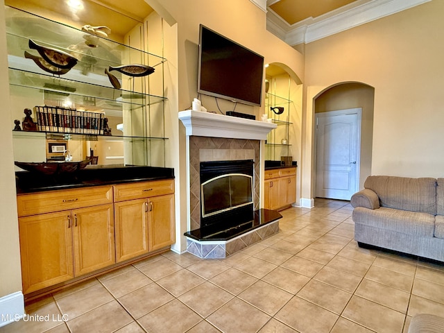 living room featuring a tiled fireplace, light tile patterned floors, arched walkways, and crown molding