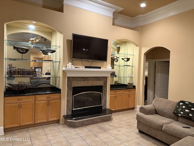 living area featuring a tiled fireplace, ornamental molding, light tile patterned floors, recessed lighting, and arched walkways