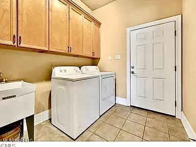 clothes washing area featuring light tile patterned floors, baseboards, cabinet space, separate washer and dryer, and a sink