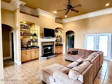 living area with a glass covered fireplace, crown molding, built in features, and arched walkways