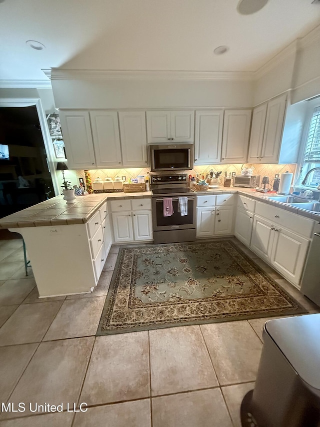 771 Versailles Dr, Ridgeland, MS 39157 - kitchen featuring appliances with stainless steel finishes, tile countertops, a sink, white cabinets, and ornamental molding