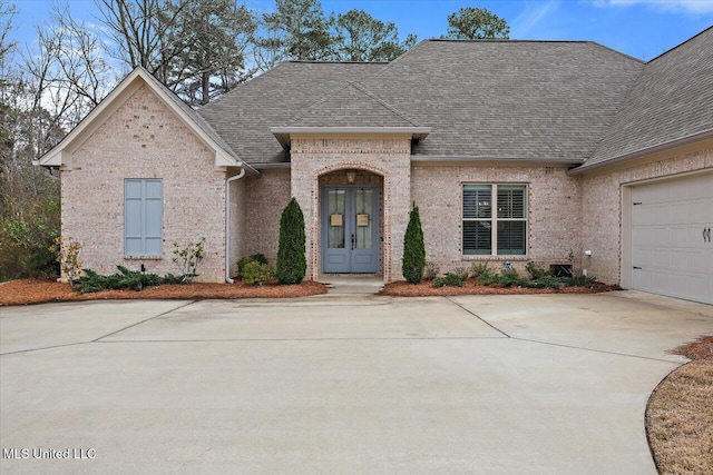 french country inspired facade featuring french doors, roof with shingles, driveway, and an attached garage