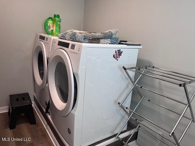 clothes washing area featuring washing machine and clothes dryer, laundry area, baseboards, and wood finished floors