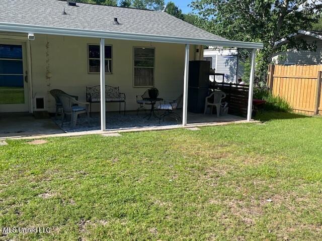 back of property featuring fence, a patio, a shingled roof, and a lawn