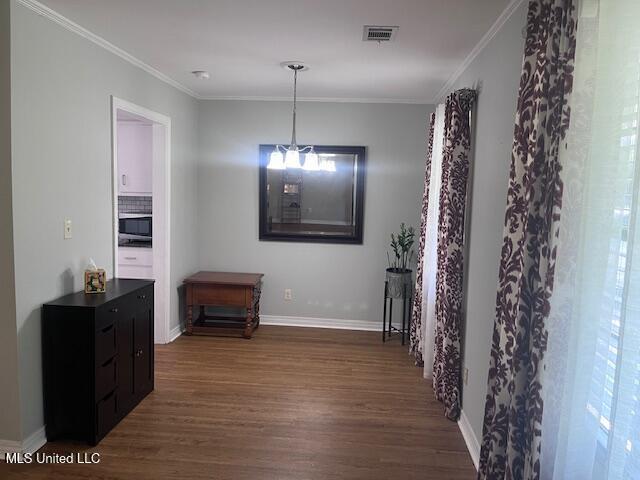 interior space with crown molding, baseboards, wood finished floors, and visible vents