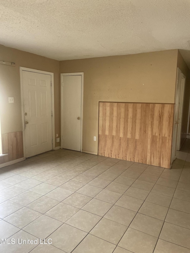 unfurnished room featuring a textured ceiling, light tile patterned flooring, wainscoting, and wood walls