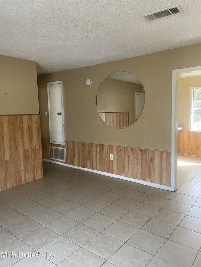 empty room featuring a wainscoted wall, a textured ceiling, visible vents, and wood walls