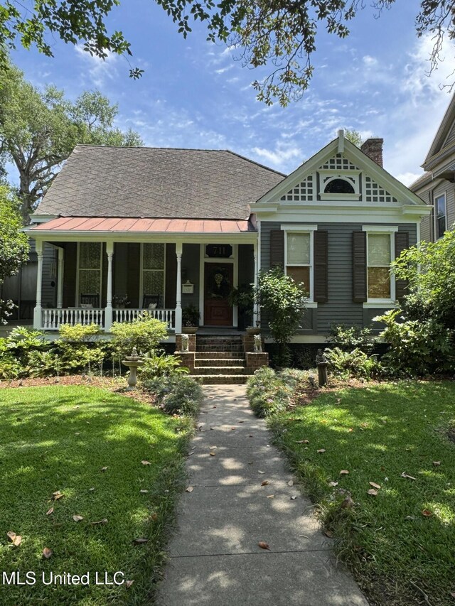 view of front facade with covered porch, a standing seam roof, a chimney, and a front lawn