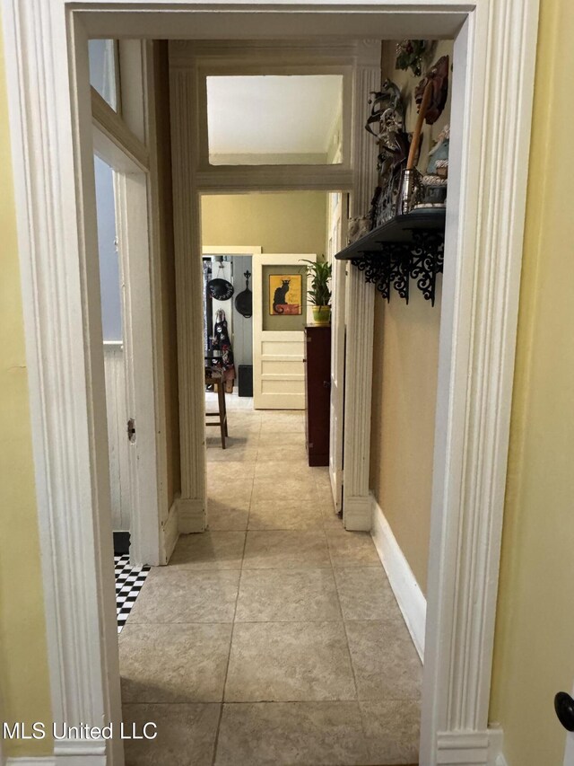 corridor with light tile patterned floors, baseboards, and ornate columns