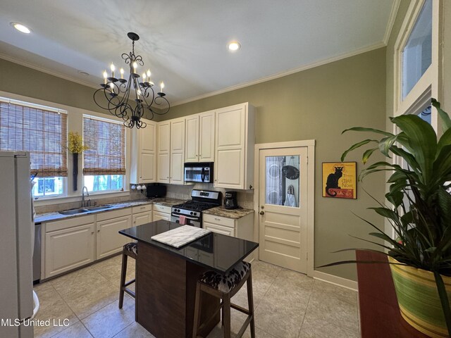 kitchen featuring freestanding refrigerator, stainless steel range with gas cooktop, a sink, light tile patterned floors, and a notable chandelier