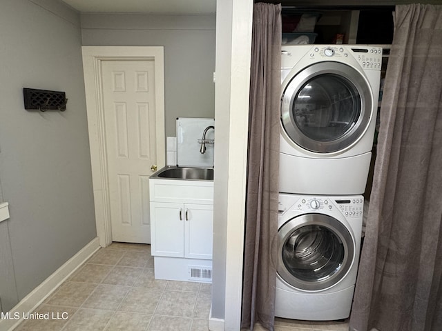 laundry area featuring laundry area, visible vents, a sink, light tile patterned floors, and stacked washer and clothes dryer
