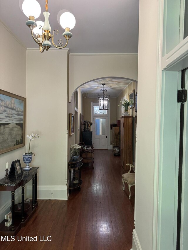 hall with arched walkways, dark wood finished floors, baseboards, an inviting chandelier, and ornamental molding