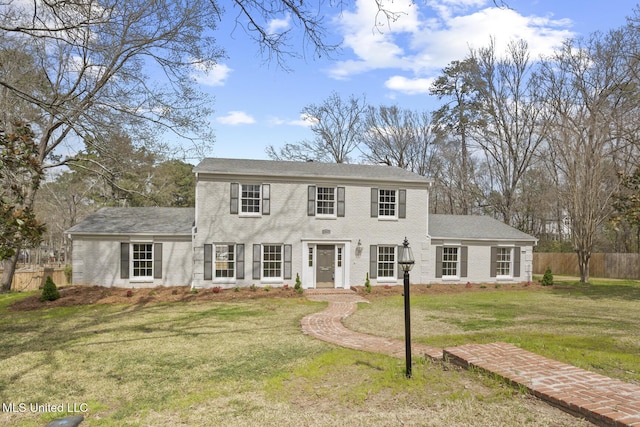 colonial home featuring brick siding, a front yard, and fence