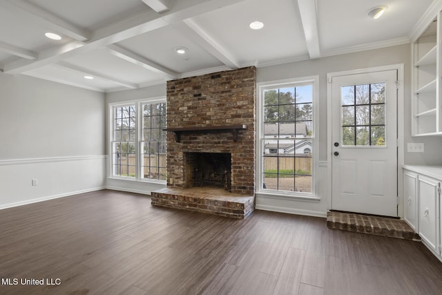 unfurnished living room featuring beamed ceiling, a healthy amount of sunlight, a brick fireplace, and dark wood-type flooring