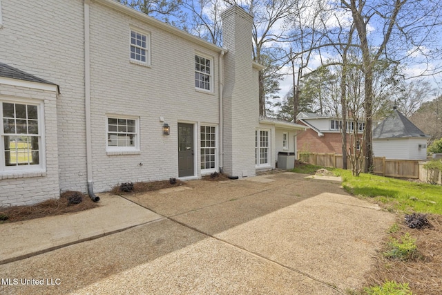 back of property with brick siding, a chimney, a patio, and fence