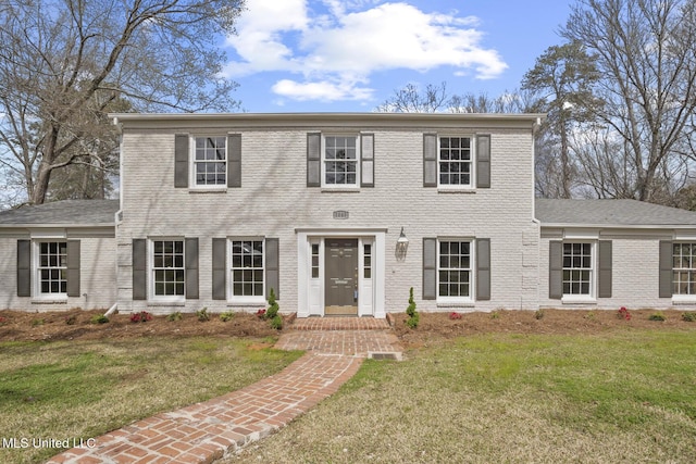 colonial inspired home featuring brick siding and a front yard