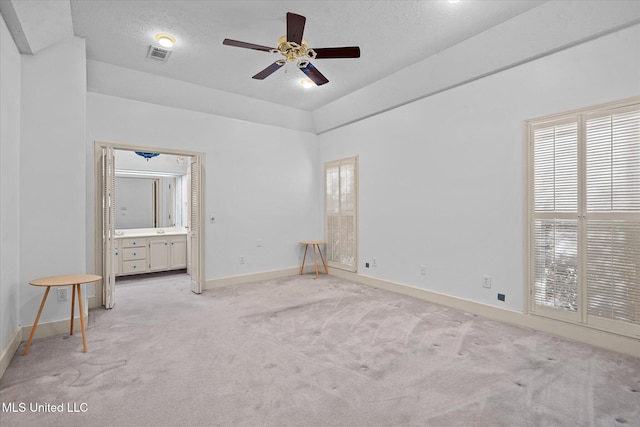 unfurnished bedroom with visible vents, baseboards, light colored carpet, a textured ceiling, and ensuite bath