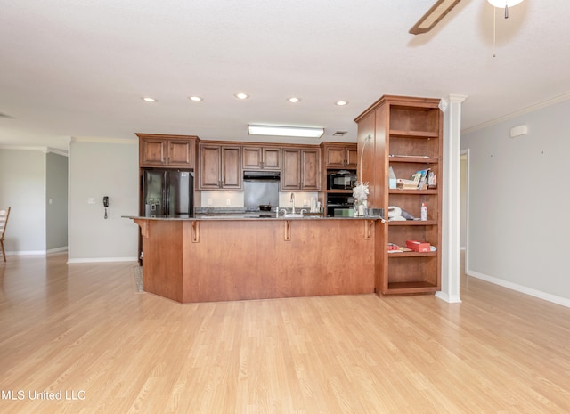 kitchen with a kitchen breakfast bar, ornamental molding, black appliances, and light hardwood / wood-style floors