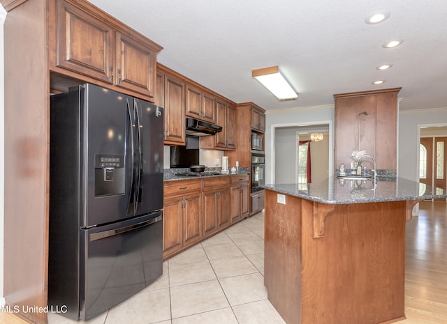 kitchen with black appliances, light tile patterned flooring, dark stone countertops, ornamental molding, and a breakfast bar area