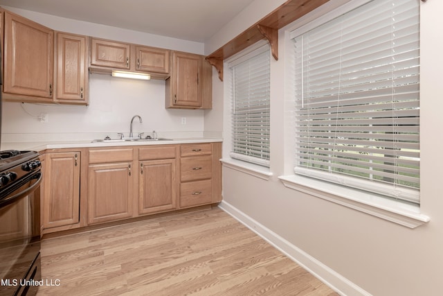 kitchen with light brown cabinets, sink, light wood-type flooring, and black stove