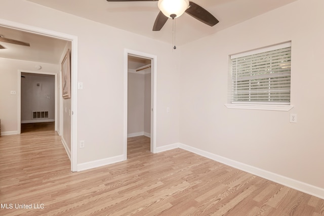 unfurnished bedroom featuring light hardwood / wood-style floors, a walk in closet, a closet, and ceiling fan