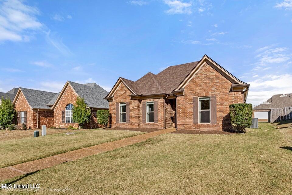 view of front of property with roof with shingles, a front lawn, and brick siding