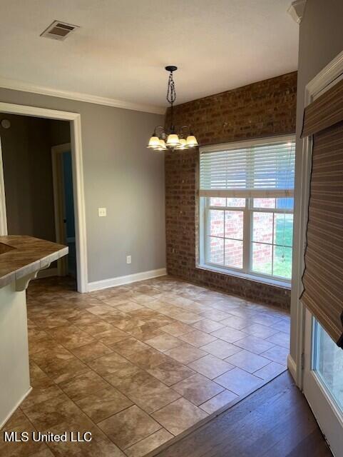 unfurnished dining area featuring ornamental molding, a chandelier, wood-type flooring, and brick wall