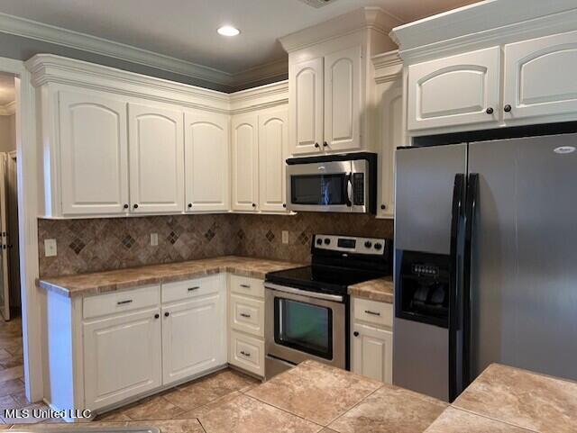 kitchen with backsplash, stainless steel appliances, ornamental molding, and white cabinets