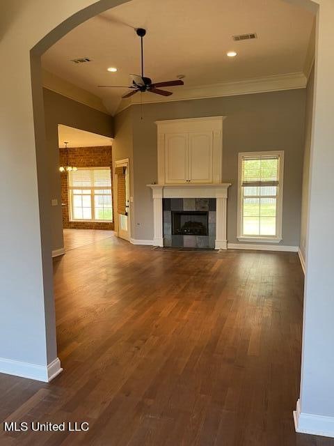 unfurnished living room with ornamental molding, ceiling fan, a tiled fireplace, and dark hardwood / wood-style flooring