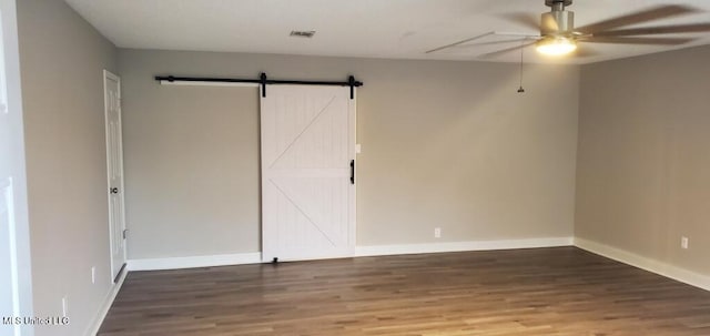 unfurnished room with visible vents, baseboards, a barn door, wood finished floors, and a ceiling fan