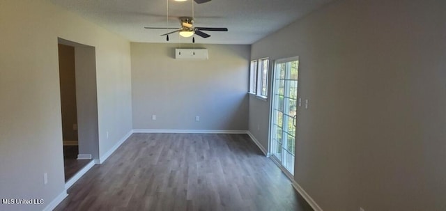 empty room with baseboards, a ceiling fan, a wall unit AC, and wood finished floors