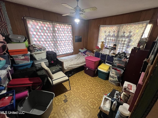 bedroom featuring ceiling fan, light floors, and wood walls